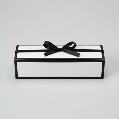 A rectangular gift box with a black frame and white interior, tied with a black satin ribbon and bow, photographed on a light gray studio background.