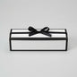A rectangular gift box with a black frame and white interior, tied with a black satin ribbon and bow, photographed on a light gray studio background.