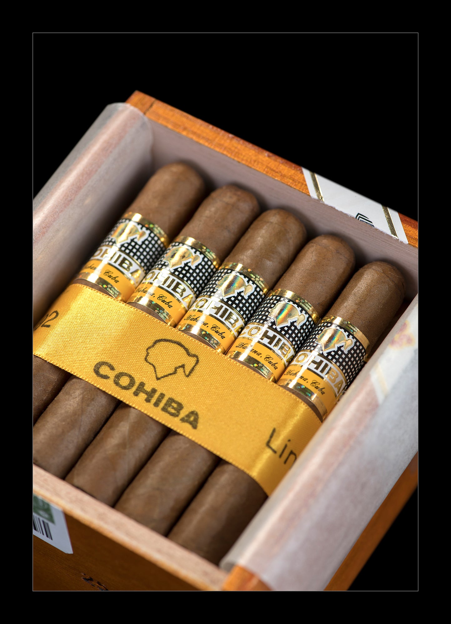 A close-up of an open Cohiba cigar box showing several brown cigars with gold and black bands, set against a black background.