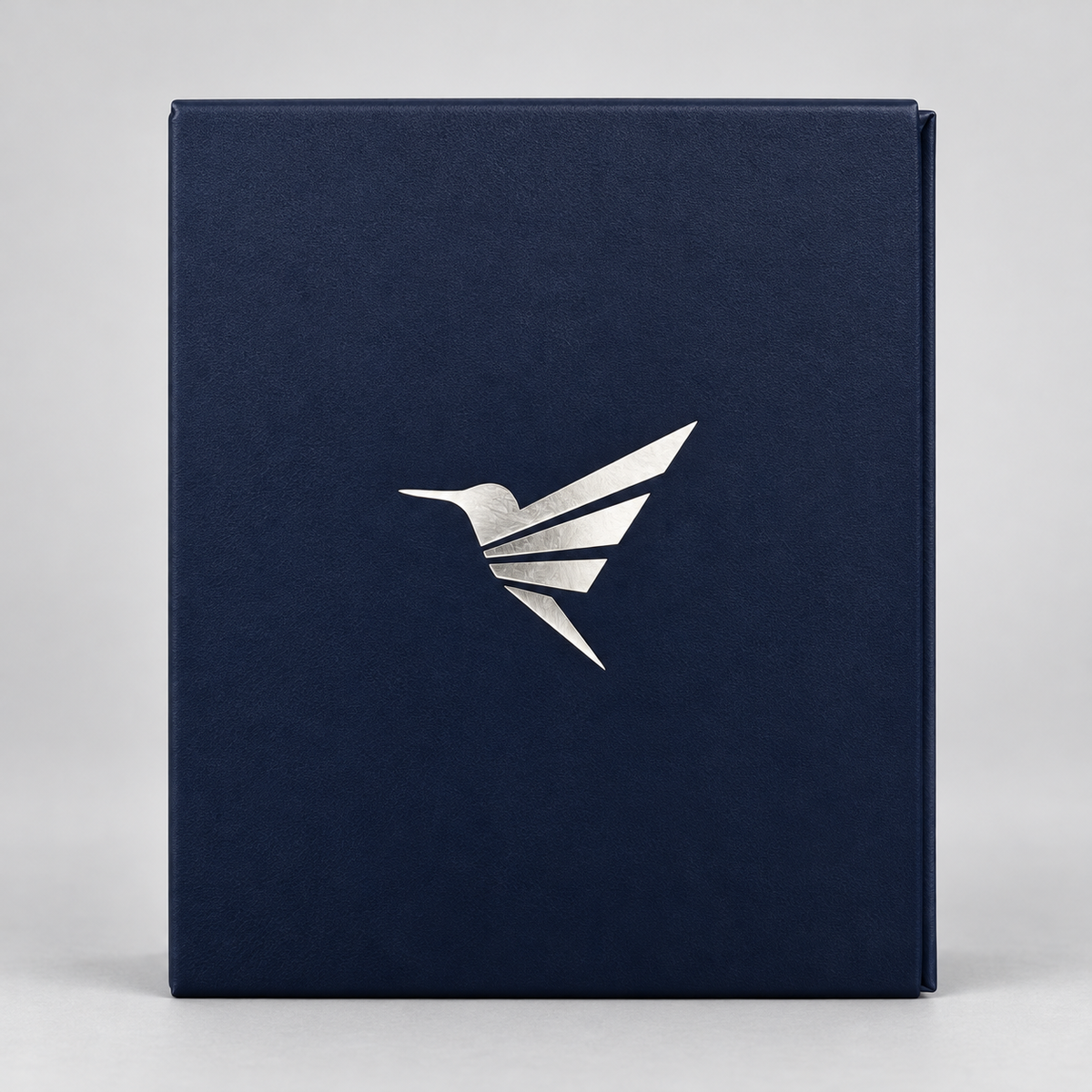 A dark navy blue textured box with a metallic silver hummingbird logo on the front, set against a neutral light gray background.