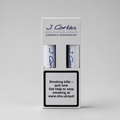 A white J. Cortés Corona Dominican tobacco packaging box on a light gray background, showing two rolled tobacco papers and a prominent smoking-health warning label on the front.