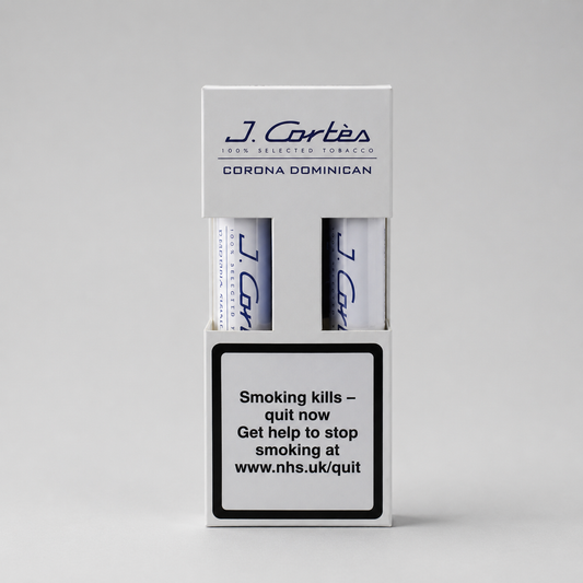 A white J. Cortés Corona Dominican tobacco packaging box on a light gray background, showing two rolled tobacco papers and a prominent smoking-health warning label on the front.