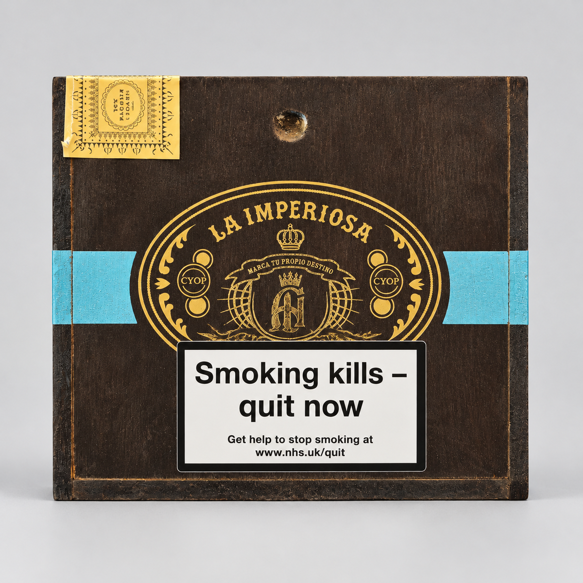 A square dark brown wooden cigar box with gold and light blue printed graphics, featuring the brand name 'La Imperiosa' and a prominent white smoking-health warning label on the front.