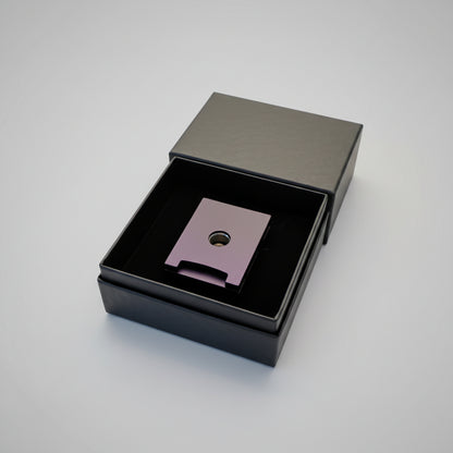 Metallic Cigar piercer with a central hole in a black box on a wooden surface