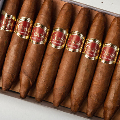 An open box of cigars arranged diagonally, showing several brown cigar bodies with red and gold bands labeled 'Cuba' and 'Hasana'.