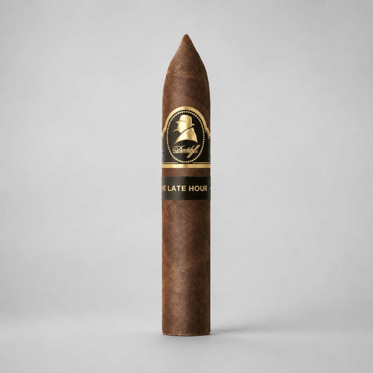 A single brown cigar standing upright on a light gray background, featuring a black and gold band with the brand name 'Don Melchor' and the text 'DE LATE HORA'.