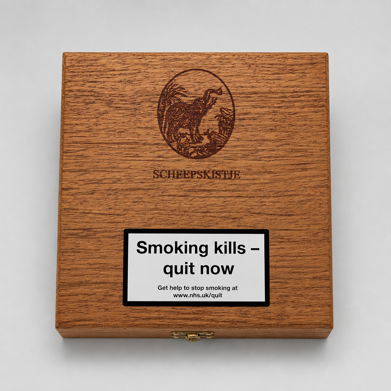 A square wooden box with a warm brown wood grain finish, featuring an engraved circular emblem and the text 'SCHEEPSKISTIFTE' above a large white smoking-health warning label that reads 'Smoking kills - quit now'. The box is photographed from above on a light gray background.