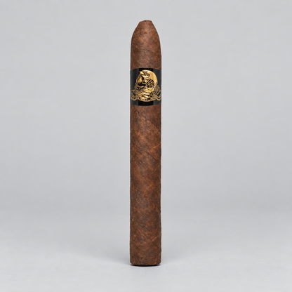 A single brown cigar standing upright against a light gray studio background, featuring a black band with a gold skull-and-crossbones design.
