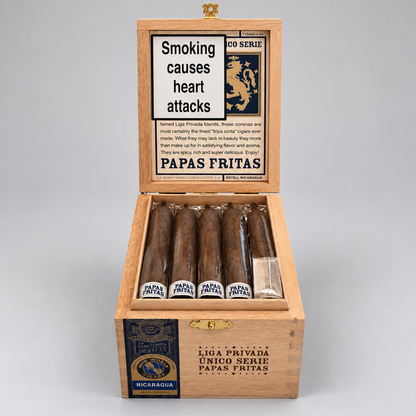 An open wooden cigar box labeled Papas Fritas, showing several cigars inside on a light gray studio background. The lid has a vintage-style panel with text about smoking and the Papas Fritas branding.