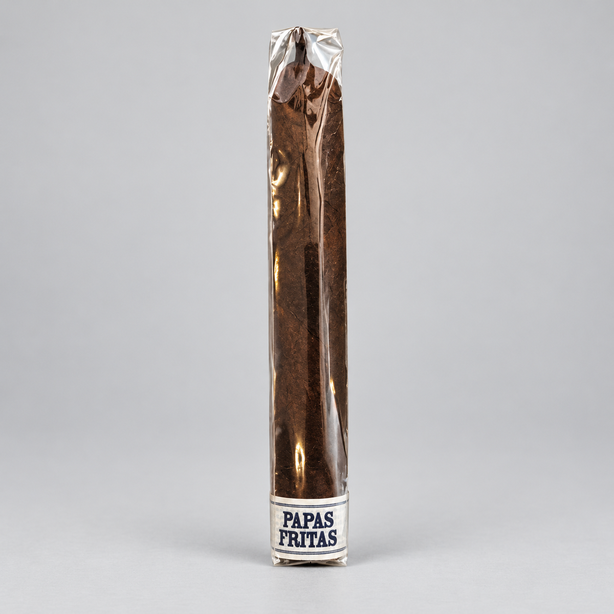 A single long cigar in a clear wrapper with a white band at the base reading 'PAPAS FRITAS', photographed upright on a light gray studio background.
