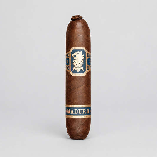 A single brown cigar standing upright on a light gray studio background, featuring a central blue and gold label with a lion emblem and the word 'MADURO' near the bottom.