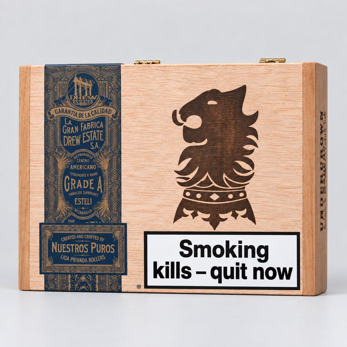 A wooden cigar box with a natural light wood finish, featuring a dark brown engraved lion head emblem, a dark blue vintage-style label on the left, and a white warning label that reads 'Smoking kills - quit now'.