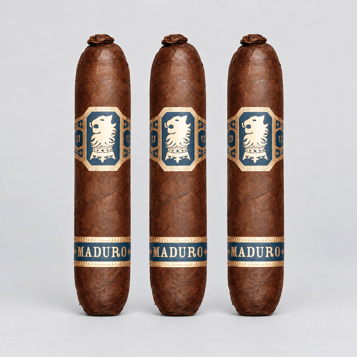 Three brown cigars standing upright against a light gray background, each with a blue and gold label featuring a white lion emblem and the word MADURO.
