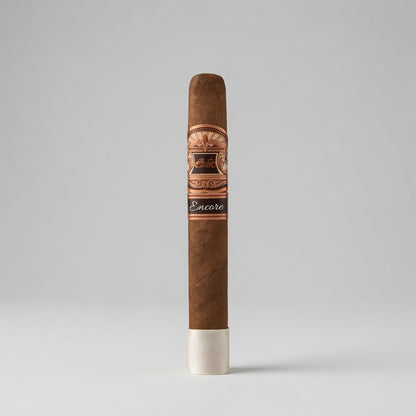 A single brown cigar standing upright on a white base against a light gray studio background. The band around the middle features a decorative gold and black design with the brand name 'Encore' visible on a dark band section near the bottom.