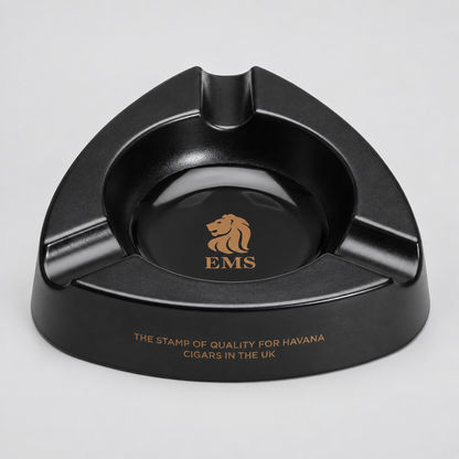 A black triangular ashtray with a glossy finish, featuring a gold lion logo and the letters 'EMS' in the center, and gold text on the front rim reading 'THE STAMP OF QUALITY FOR HAVANA CIGARS IN THE UK'.