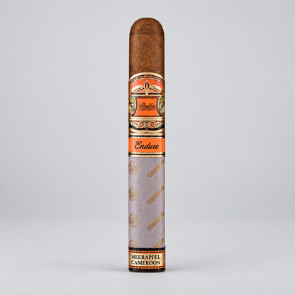 A single cigar in its paper sleeve, standing upright against a light gray background. The cigar is labeled 'Endure' and 'Meerappel Cameroon'.