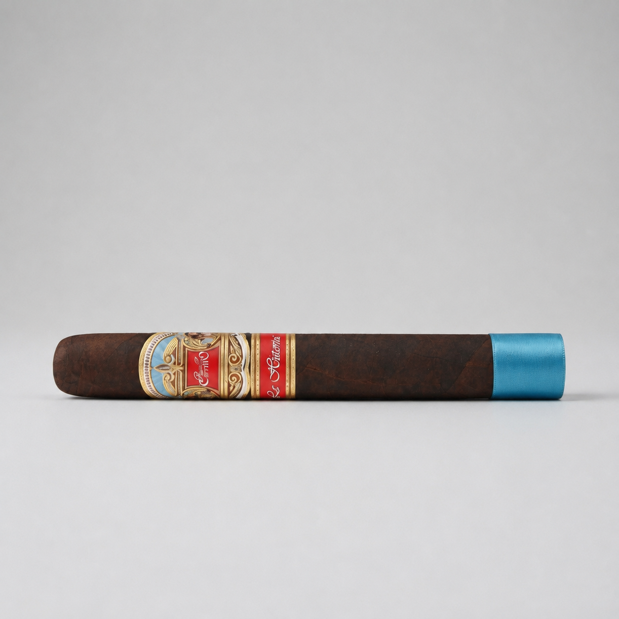 A single dark brown cigar with a detailed gold, red, and blue band, and a metallic blue tip, shown horizontally against a neutral gray background.