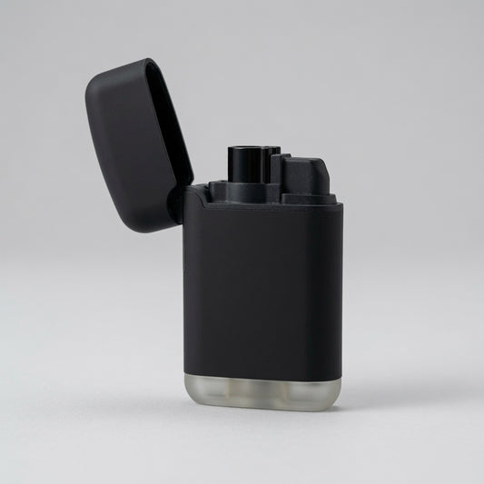 A matte black electronic lighter with its lid open, standing on a light gray surface against a neutral gray background.