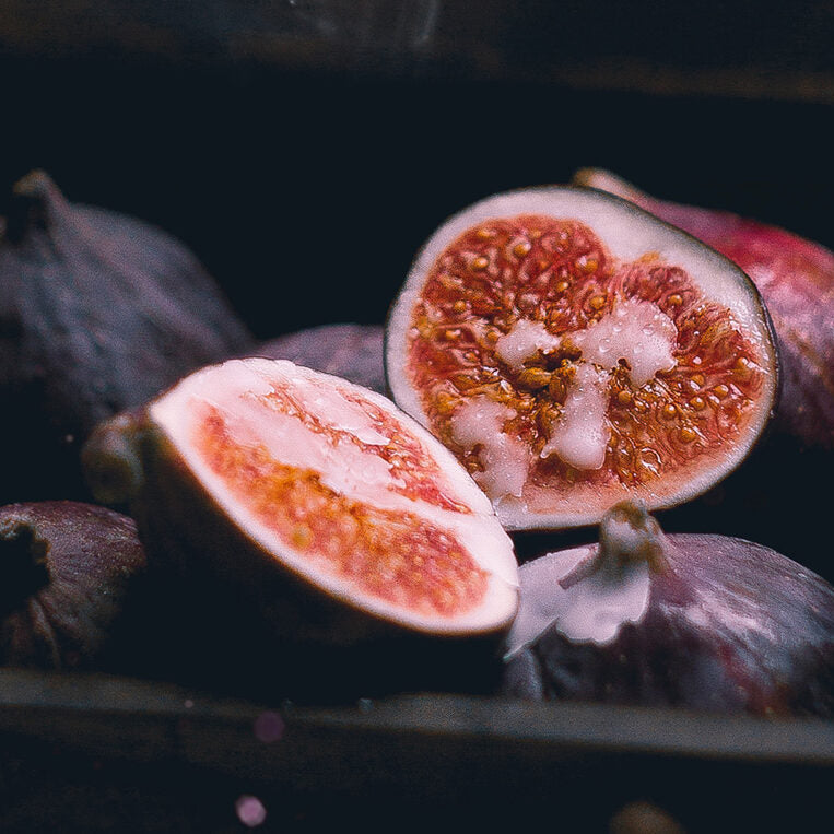 Figs, including a sliced one, on a dark surface with a wooden box.