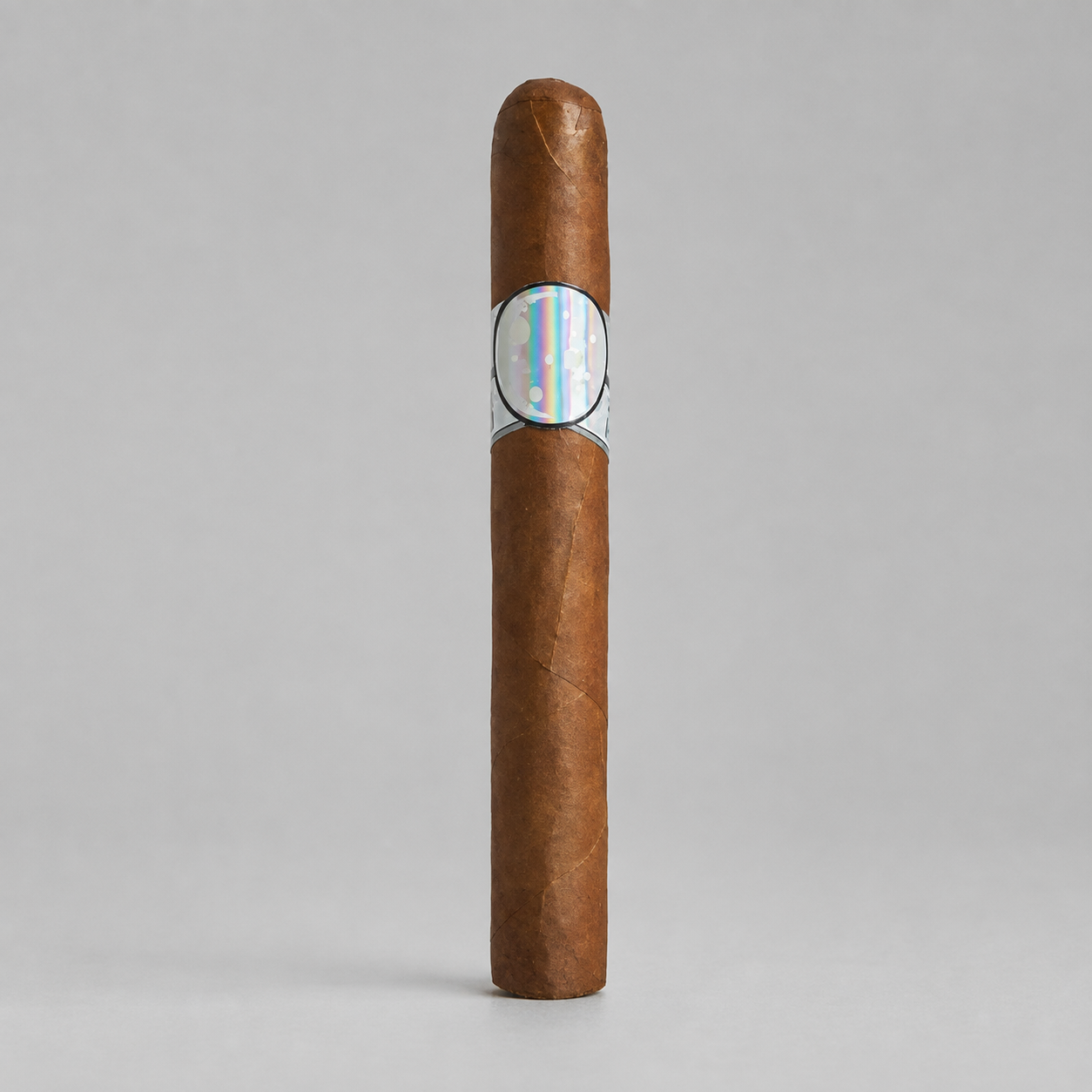 A single brown cigar standing upright on a light gray background, featuring a silver band with a colorful iridescent map design in the center.