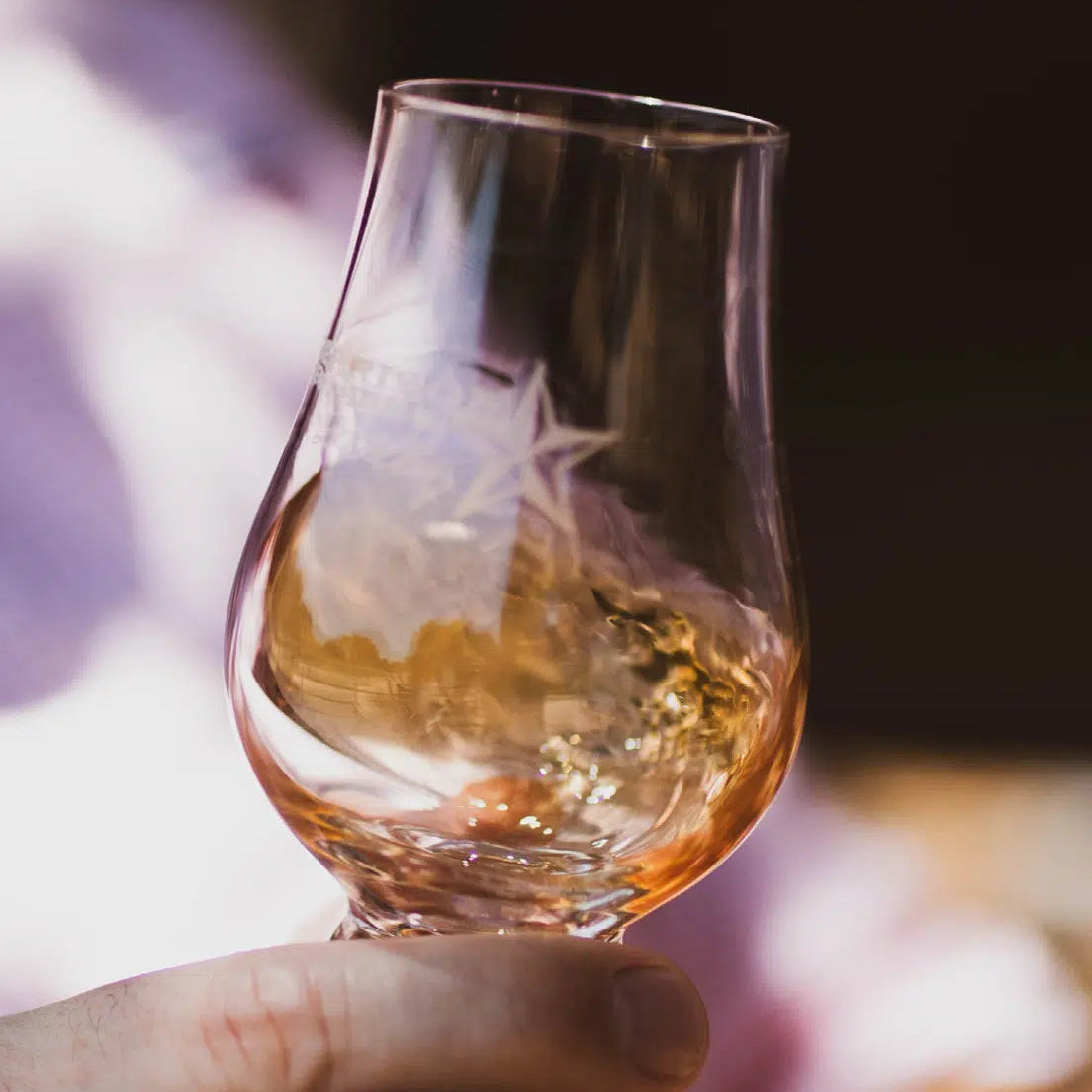 Hand holding a whisky glass with a blurred background