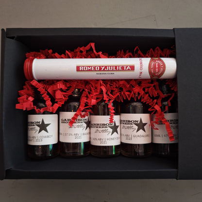 Set of miniature bottles of Garrison Brothers whiskey with labels and a tube labeled 'Romeo y Julieta' in a black box.