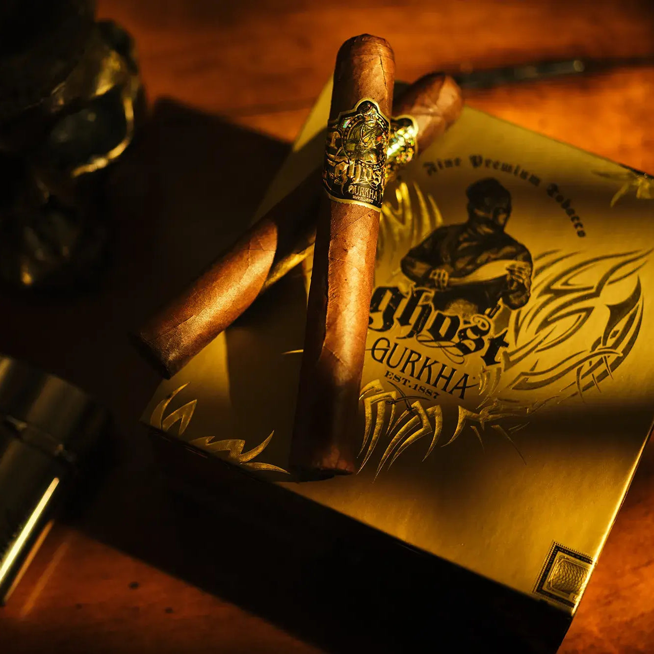 Gold box of Ghost Gurkha cigars with a cigar and lighter on a wooden surface