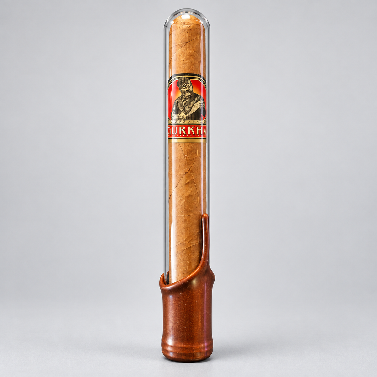 A single cigar in a clear cylindrical protective case with a brown leather base, photographed upright on a light gray studio background. The cigar band shows the brand name BURKH.