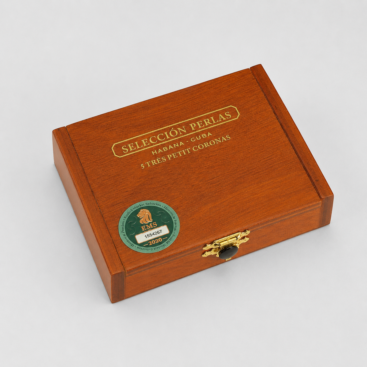 A rectangular wooden cigar box with a warm reddish-brown wood grain finish, featuring gold-etched text reading 'SELECCION PERLAS' and a round green-and-gold sticker on the lid, photographed on a light gray studio background.