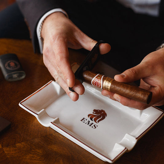 Person cutting a cigar with a glass of Havana Club rum on a wooden table.