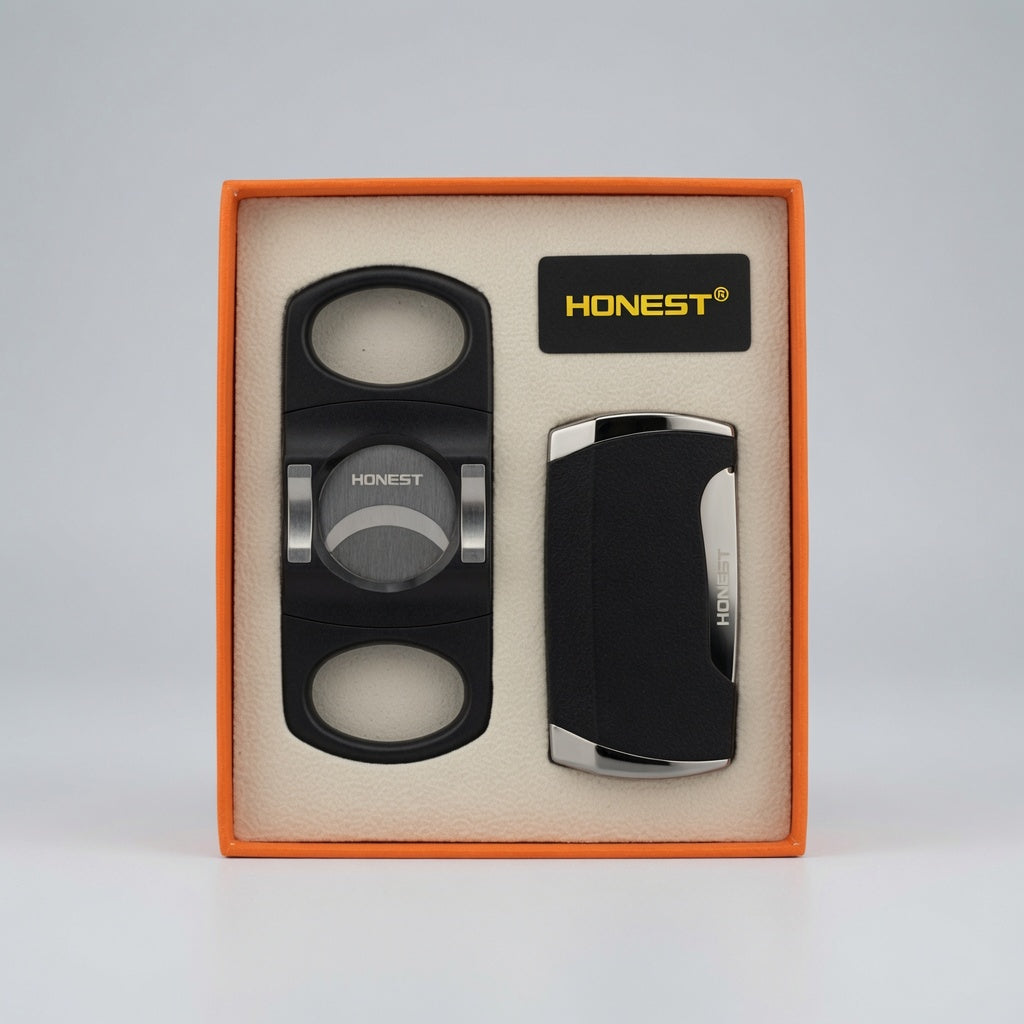 A cigar accessory gift set by Honest, including a black cigar cutter with silver accents and a black lighter with a silver side trim, presented in an orange box with a beige insert.