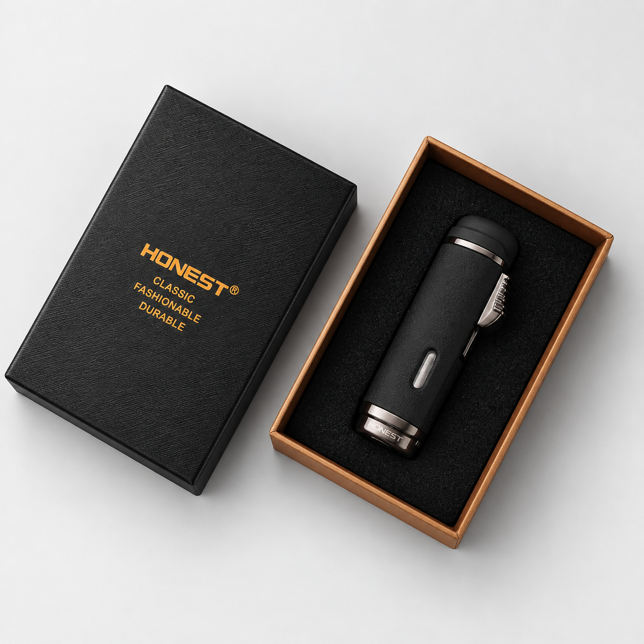 A black cylindrical Honest Cigar lighter with punch displayed inside an open rectangular presentation box next to its closed black lid, which is printed with the brand name HONEST in gold.