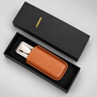 A silver metallic pocket CIGAR POUCH with a tan leather sheath, presented in an open black gift box next to its closed lid, which features the brand name 'HONEST' in gold.
