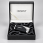 A black and silver Honest lighter resting on a black satin cushion inside an open black presentation box with a white interior and the Honest logo printed on the lid.