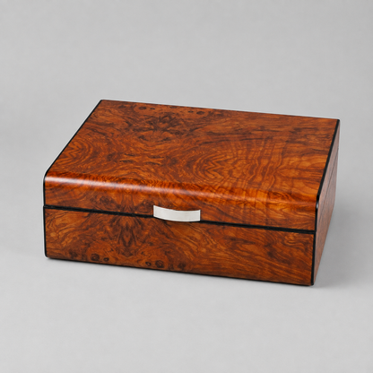 A rectangular wooden box with a rich burl wood grain finish in warm reddish-brown tones, featuring a small silver metal handle on the front, set against a neutral gray background.