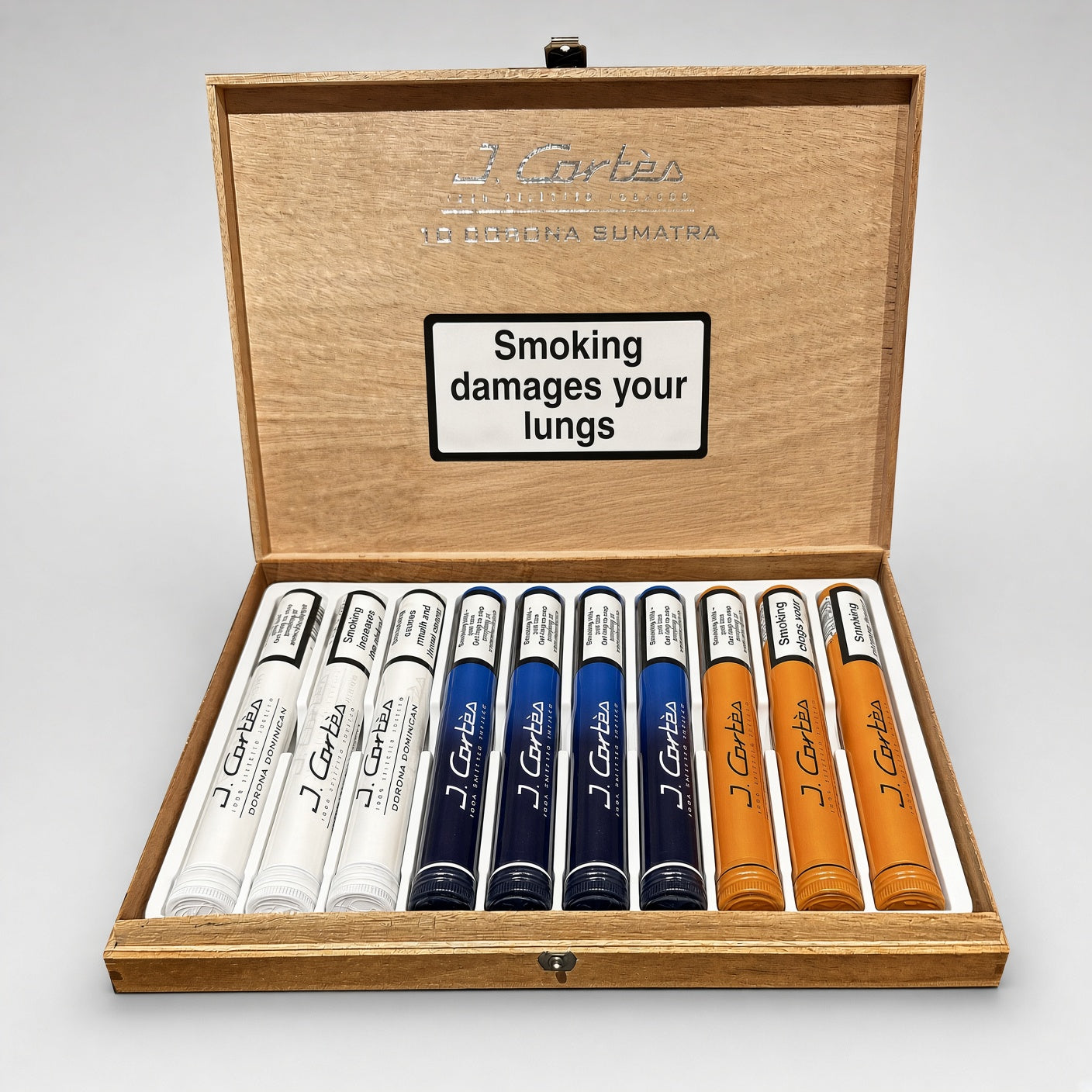 An open wooden presentation box containing several tubed cigars in white, blue, and orange, with the brand name J. Cartes visible on the devices and inside the lid.
