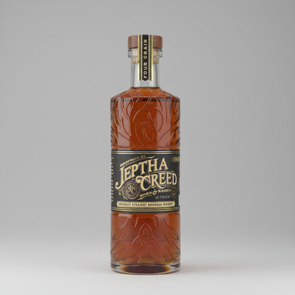 A bottle of Jethta Creed Bourbon Mash Ball spirit, featuring an amber-colored liquid inside a clear glass bottle with embossed floral patterns, a black label with gold lettering, and a dark brown cap.