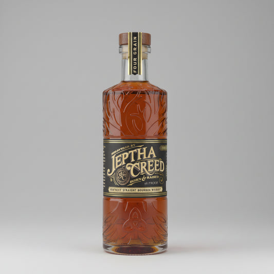 A bottle of Jethta Creed Bourbon Mash Ball spirit, featuring an amber-colored liquid inside a clear glass bottle with embossed floral patterns, a black label with gold lettering, and a dark brown cap.
