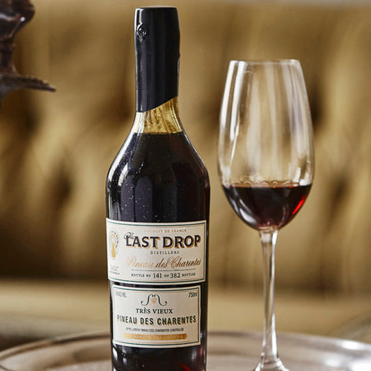 Bottle of LAST Drop 23 on a tray with a glass of wine in the background