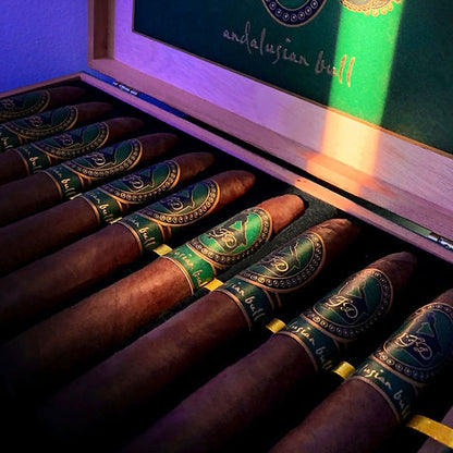 An open wooden cigar box containing several dark brown cigars with green and gold bands. The inside lid features a green panel with gold decorative graphics and the text 'andalusian bull'.