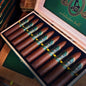 An open wooden cigar box filled with brown cigars, each with a green and gold band. The inside lid is green with gold script reading 'andalusi ball' and a circular logo.