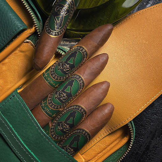Four cigars with ornate green and black bands displayed inside a green and tan leather cigar case.