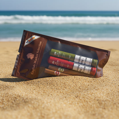A packaged set of smoking accessories on a white marble-like surface, including a brown pouch labeled 'English Market Selection' with three rolling papers tubes in green, red, and white, and four brown cigars inside.