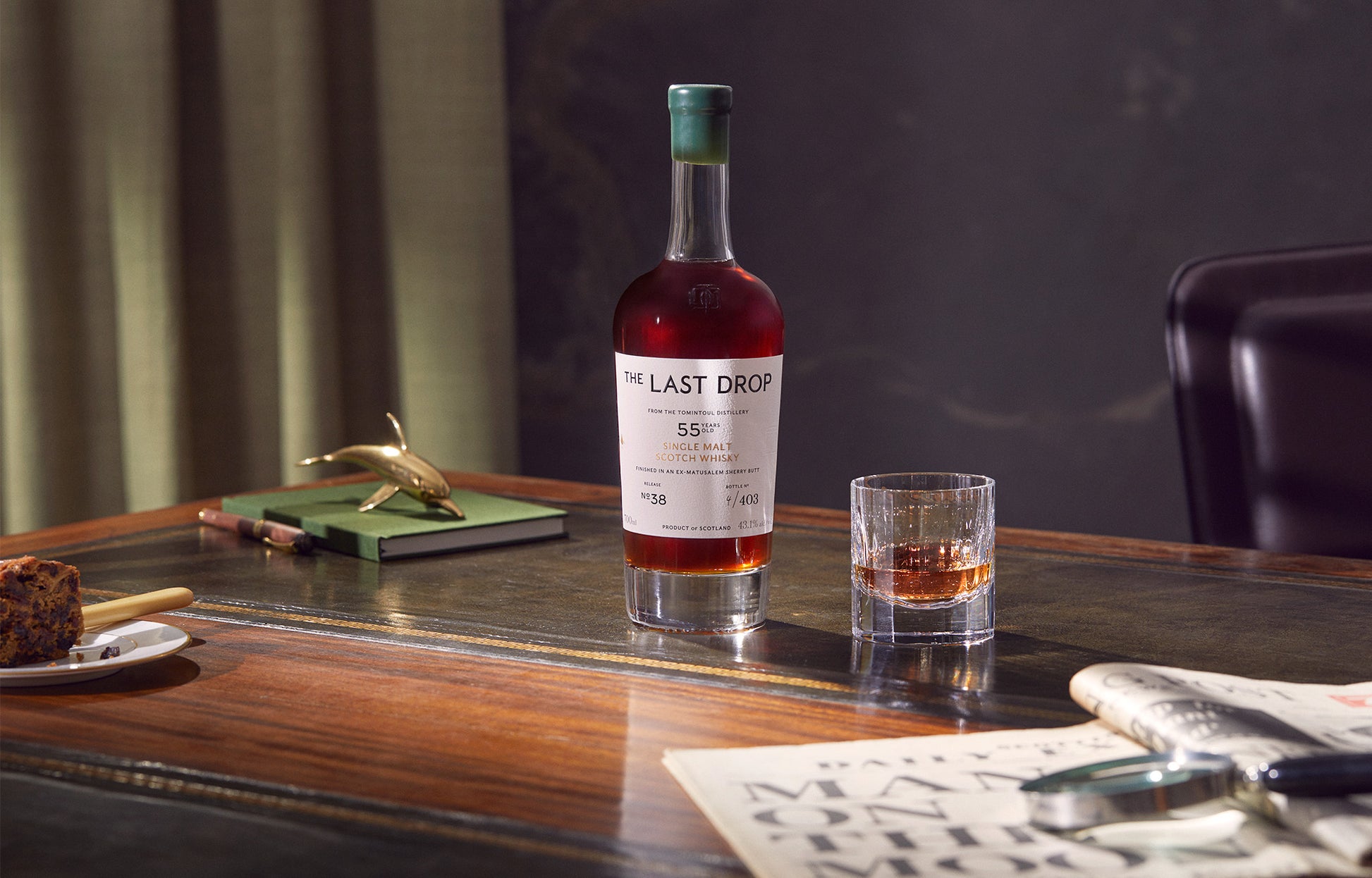 Bottle of 'The Last Drop' whiskey on a wooden table with a glass of whiskey.