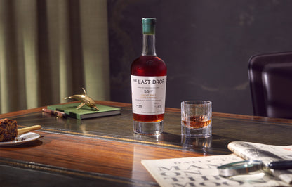 Bottle of 'The Last Drop' whiskey on a wooden table with a glass of whiskey.