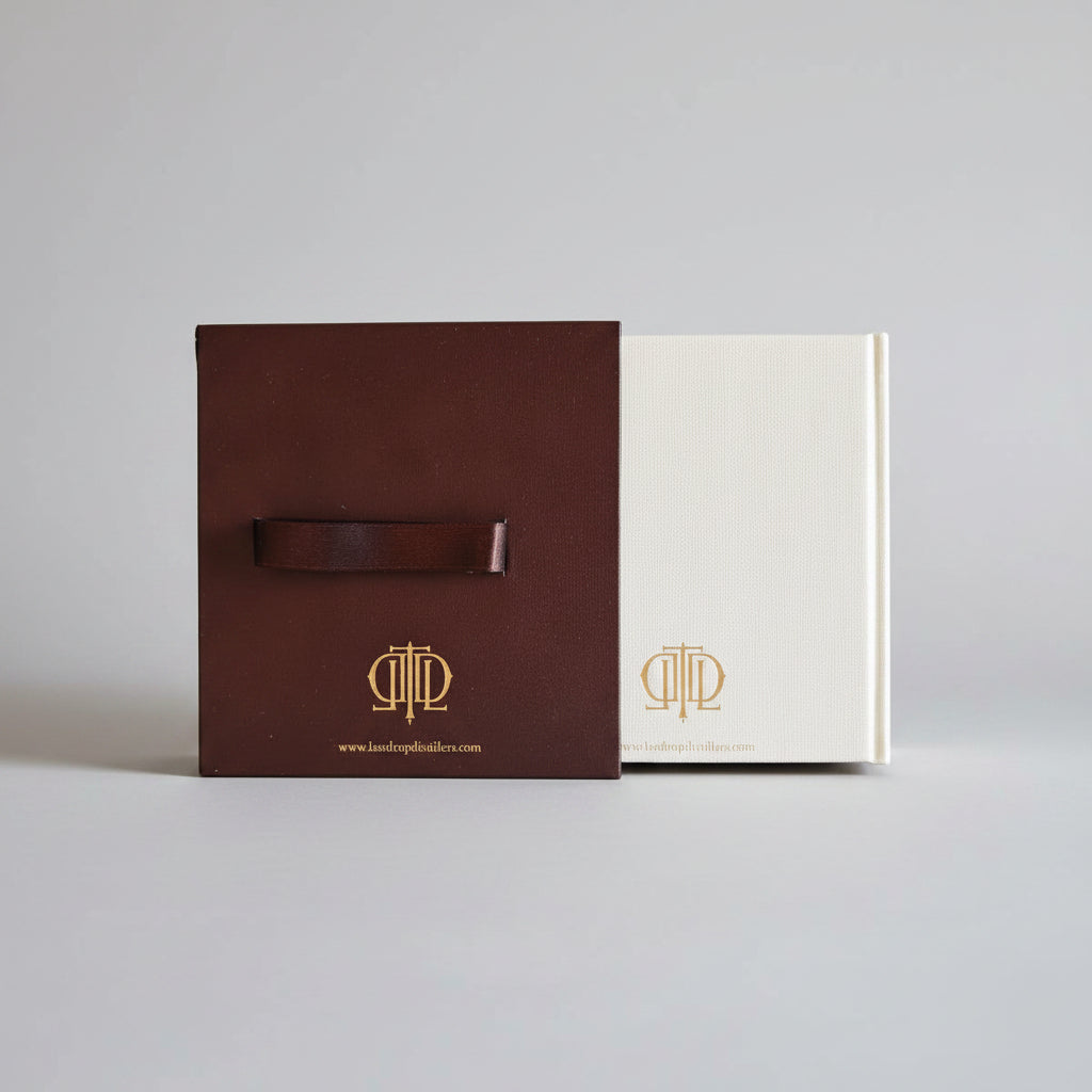 A brown leather strap with a gold logo attached to a dark brown rectangular box, placed on top of a cream-colored booklet or card, all on a textured blue background.