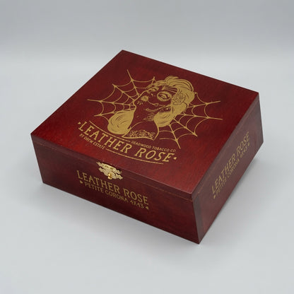 A square dark red wooden box with gold laser-engraved artwork of a woman's face inside a spiderweb and the text 'LEATHER ROSE' and 'SMOKING TOBACCO CO.', photographed on a light gray studio background.