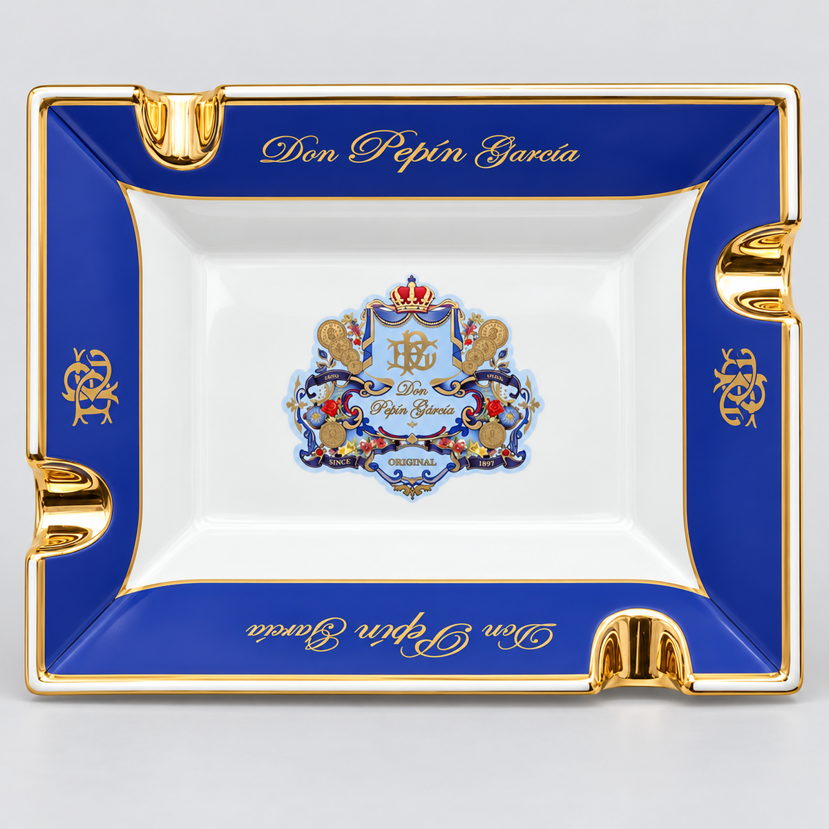 A square white porcelain ashtray with a royal blue border and gold trim, featuring the 'Don Pepin Garcia' brand name in gold script and a detailed crest in the center.