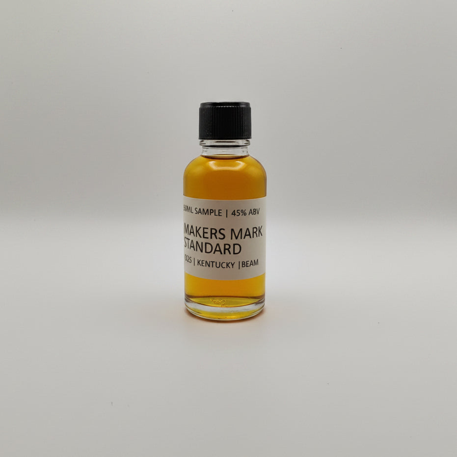 Bottle of Maker's Mark whiskey sample on a white surface with two silver bags in the background.