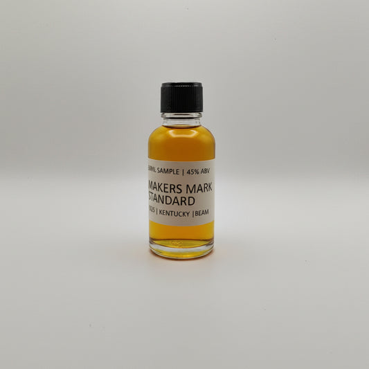 Bottle of Maker's Mark whiskey sample on a white surface with two silver bags in the background.